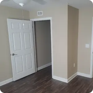 Empty room with hardwood floors and white door, minimalistic design, natural light coming in from window.